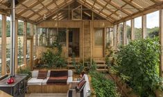 a living room filled with furniture and lots of plants inside of a wooden structure covered in windows