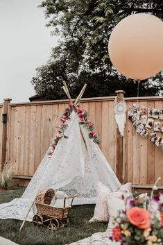 a teepee tent with flowers and decorations on the grass near a wooden fence in front of a balloon