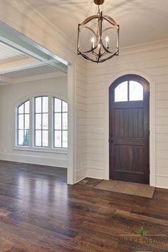 an empty room with a chandelier hanging from the ceiling and wood flooring