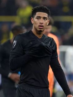 a soccer player is walking on the field with his hand in his pocket and people behind him