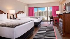 two beds in a hotel room with pink drapes on the windows and city view