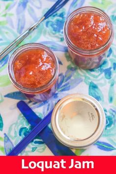 two jars filled with jam sitting on top of a table next to blue spoons