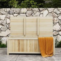 a wooden bench sitting in front of a stone wall with an orange towel on it