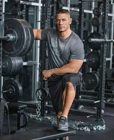 a man squatting on a bench in a gym with barbells behind him