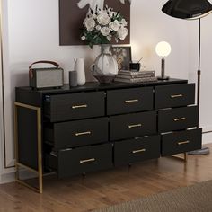 a black dresser with gold handles and drawers in front of a painting on the wall