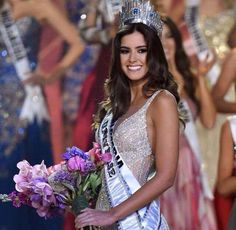 a woman in a silver dress holding a bouquet of flowers and wearing a tiara