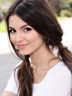 a beautiful young woman sitting on top of a wooden bench smiling at the camera with long hair