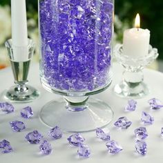 purple crystals in a glass vase on a table with two candles and one candle holder