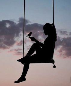 the silhouette of a woman sitting on a swing with a bird perched on her leg