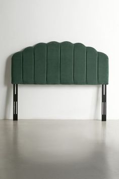 an upholstered headboard with black legs and green velvet fabric, against a white wall