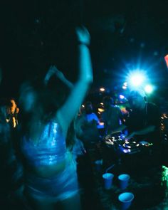 a group of people dancing in the dark at an outdoor party with bright lights on them