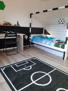 a bedroom with a bed, desk and soccer themed rugs on the wooden floor