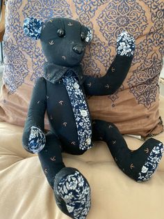 a black teddy bear sitting on top of a bed next to a blue and white pillow