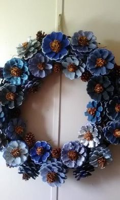 a wreath made out of blue flowers and pine cones is hanging on the front door