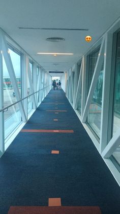 an empty walkway with people walking down it in the distance and windows on both sides