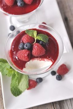 two glasses filled with fruit and ice cream on top of a white plate next to mint leaves