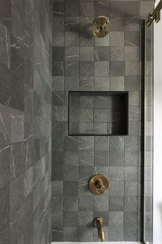 a bathroom with gray tiles and gold fixtures on the shower wall, along with two brass faucets