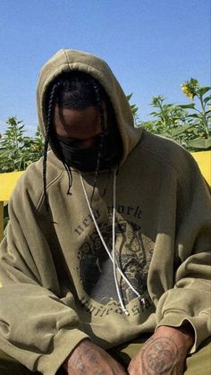 a man with dreadlocks sitting on a bench wearing a hoodie and looking at his cell phone