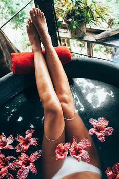 a woman laying down in a hot tub with flowers on the bottom and her legs