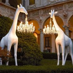 two white giraffe statues with chandeliers in front of a building