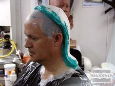 a man is getting his hair cut in the barber shop while another man looks on