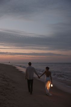 a man and woman holding hands while walking on the beach at sunset with their arms around each other