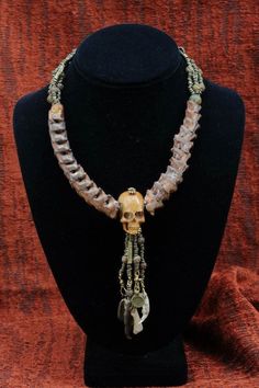 Primitive Modern Necklace - Bone and carved skulls, Snake Bone Vertebrae. Artist: Teresa Bradford-Cole Danbala Wedo  Ethiopian spacer beads, classic brass beads are inspired by gold beads produced by Ashanti and Baoule people in west Africa, Charms of Brass Hand, chicken toe, fox toe bone, Rat jaw and tooth, ah yes Buddha The term Buddha means "Awakened". As he fully comprehended the Four Noble Truths and as he arose from the slumbers of ignorance he is called a Buddha. Since he not only comprehends but also expounds the doctrine and enlightens others, He is called a Samma-Sambuddha --a Fully Enlightened One. Snake Vertebrae, White Tail Deer Antler,chicken toe, yack tooth, rat Jaw.   $420- Necklace Measurements:  Neckline: 16" Center piece: 1 1/4" x 3/4" Centerdrop: 3 1/2" * Looking for mo Carved Skulls, Statement Piece Jewelry, Fancy Hands, Amulet Charm, Modern Necklace, Talisman Necklace, Brass Hand, Pacific Grove, Beaded Handbag