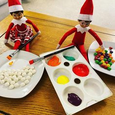 two elfs are painting on plates with candy and marshmallows in front of them