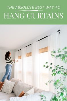 a woman standing on top of a couch in front of a window with the words, the absolute best way to hang curtains