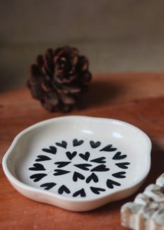 a white bowl sitting on top of a wooden table next to a small pine cone