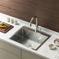 a stainless steel kitchen sink on a marble countertop next to dishes and napkins