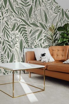 a living room with a couch, coffee table and plant wallpaper on the walls