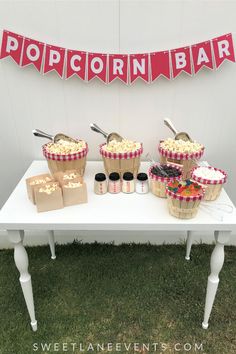 a table topped with lots of cupcakes next to a sign that says popcorn bar