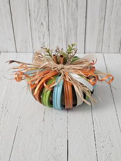 a small pumpkin decorated with ribbons and flowers on a white wooden surface, ready to be used as an ornament