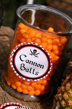 a jar filled with orange candies sitting on top of a table next to a pineapple