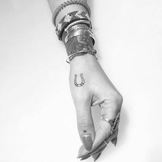 a woman's hand with a horseshoe tattoo on her left thumb and bracelets around her wrist