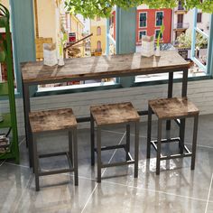 three stools sit at a table in front of a window with a mural on the wall behind it