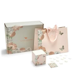 a pink gift bag and its contents are shown in front of the box with butterflies on it