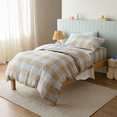 a bed with plaid sheets and pillows on top of it next to a wooden floor