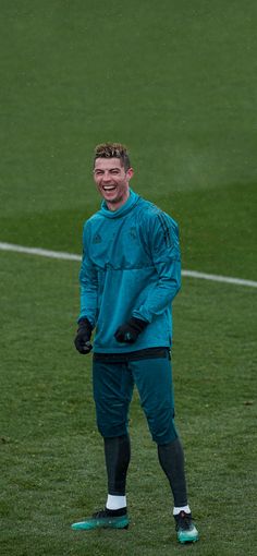 a man standing on top of a soccer field wearing blue and black clothes with his hands in his pockets