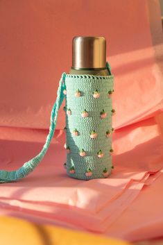 a crocheted water bottle cover is shown on a pink sheet with a silver lid