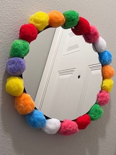 a mirror that has some pom poms on the rim and is hanging on a wall