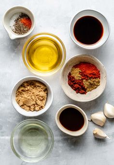 bowls filled with spices and seasonings on top of a white countertop next to garlic