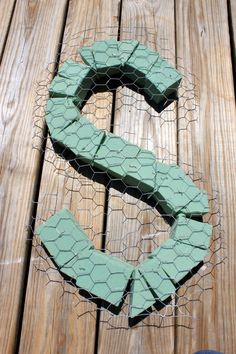 a piece of chicken wire sitting on top of a wooden floor next to a green letter