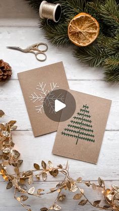 two christmas cards sitting on top of a table next to some scissors and other decorations