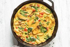 an omelet with mushrooms, spinach and tomatoes in a cast iron skillet