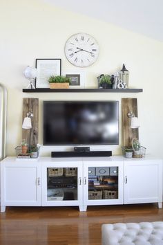 a white entertainment center with a large clock on the wall above it and shelves below