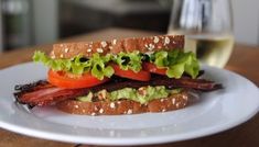 a sandwich with bacon, lettuce and tomatoes on it sitting on a plate