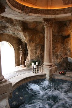 an indoor hot tub is shown with candles on the side and statues in the background