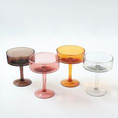 four different colored wine glasses sitting next to each other on a white surface with one empty glass in the middle